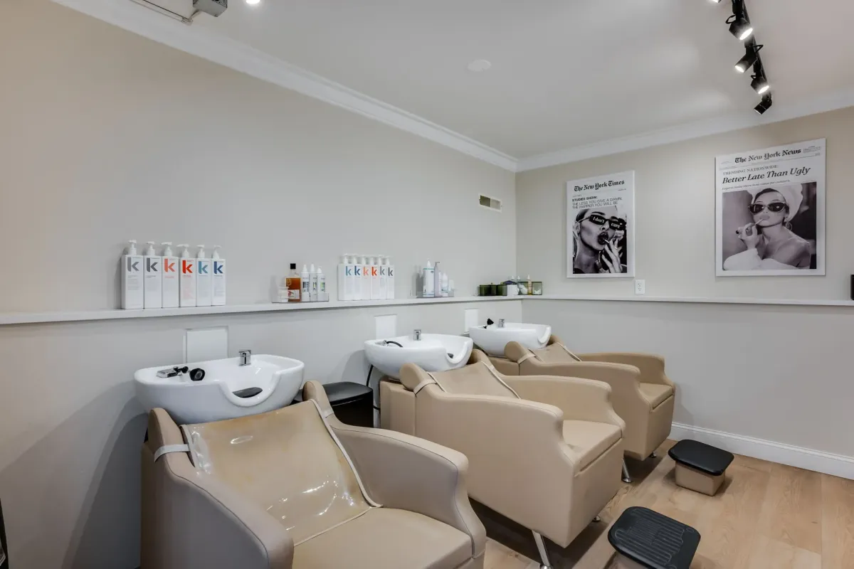 Professional salon shampoo bowl area with beige chairs and product display